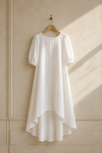 White linen high-low midi dress, hanging on wooden hanger against plaster wall